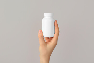 Woman holding blank white jar of vitamins on light grey background, closeup. Space for text