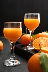 Tasty tangerine liqueur in glasses and fresh citrus fruits on black textured table