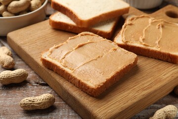Tasty peanut butter sandwiches and peanuts on wooden table, closeup