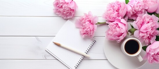 Beautiful bright pink flowers peonies and a notebook with a cup of coffee on a white wooden background.