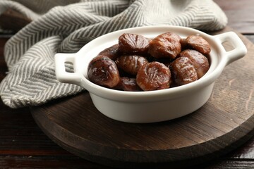 Roasted edible sweet chestnuts in dish on light wooden table