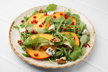 Tasty salad with persimmon, blue cheese, pomegranate and walnuts served on white tiled table