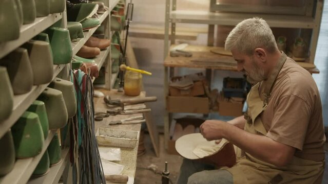 Professional senior shoemaker using glue while making leather boots in cobbler workshop