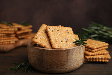 Cereal crackers with flax, sesame seeds and rosemary in bowl on wooden table, closeup