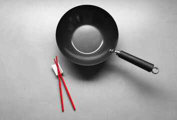 Empty iron wok and chopsticks on grey table, flat lay
