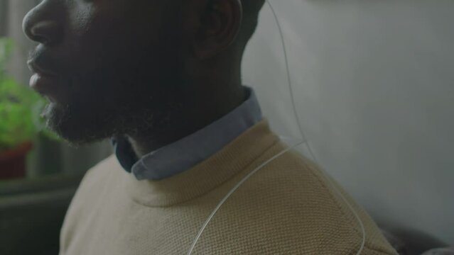 Close up tilt down shot of African American patient with electrodes on his temples sitting with eyes closed during electroencephalogram procedure in sleep clinic