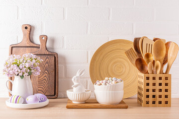 Fototapeta na wymiar Kitchen wooden countertop with kitchen utensils and festive decorations for the spring Easter holiday. Front view. White brick wall.