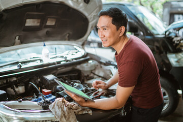 car mechanic using a tablet digital to checking up on car engines parts for fixing at workshop