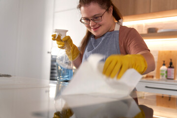Down syndrome woman cleaning worktop in domestic kitchen