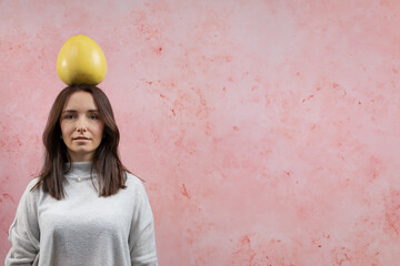 Woman looking upside with whole pomelo fruit on her head. Equilibrium concept. Pink textured...