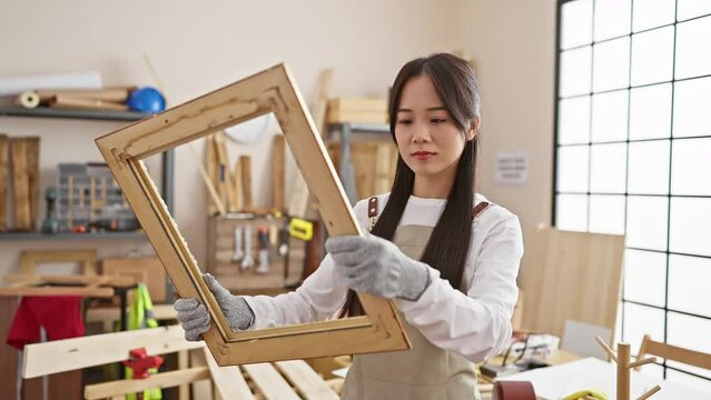 A focused asian woman examines a wooden frame in a well-lit carpentry workshop