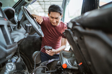 A male mechanic uses a scan tool to determine engine damage under the car seat