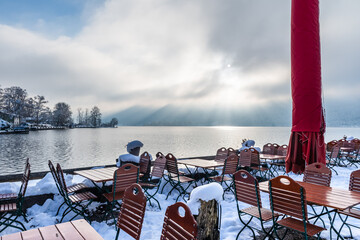 Snow-covered tables and chairs of a cafe on the shore of Lake Schliersee in the German Alps