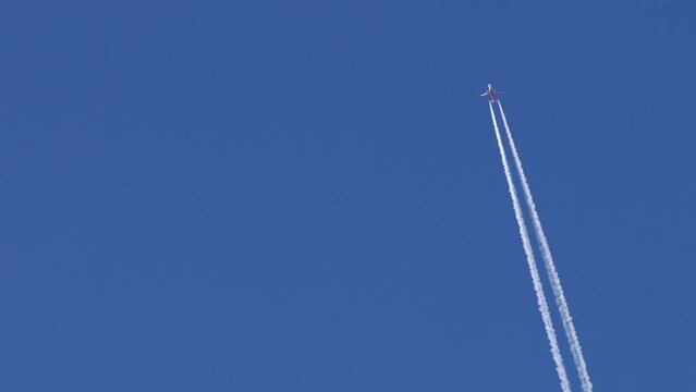 The journey begins, plane flies high in the sky, leaving a white trail. Jet airplane flying overhead in clear blue sky and leaving nice contrail. Plane smoothly as it flies through the sky