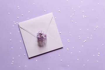 Square envelope, lilac flowers and petals on a lilac plain background. Beautiful flowers composition. Valentines Day, Easter, Birthday, Happy Women's Day, Mother's day. Flat lay, copy space, top view