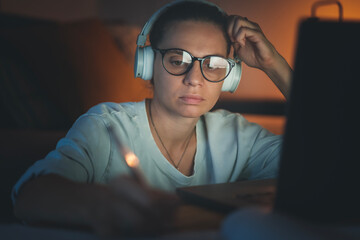 Young woman working at home at night on a project using a laptop. Online education