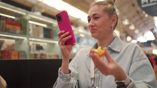 Beautiful young tourist using smartphone while eating Portuguese dessert in market. Happy woman enjoying traditional dessert Pastel de Nata in city. Blond female is on vacation.