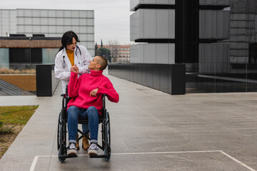 A woman with cancer sits in a wheelchair while being pushed by her oncology doctor.