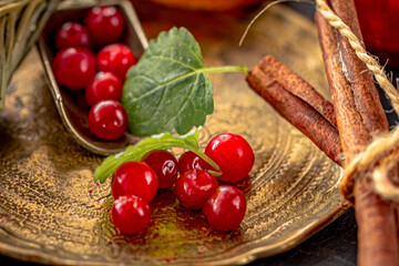Fresh lingonberries, green leaves and cinnamon sticks on metal plate on dark.  Nordic berry, superfood, superfruits, health benefits