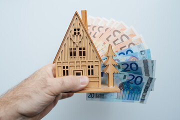 a man warmly embraces a small, wooden dream house adorned with Japanese fan-shaped banknotes, symbolizing his aspirations for property ownership, real estate investment, or renting.