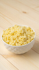 Millet porridge in white cup on wooden background, selective focus, vertical photo