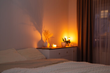 burning candles with flowers in vase in bedroom at night