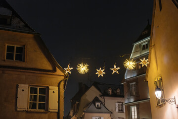 A real scene captures star decorations adorning the city of Strasbourg, France, Alsace, with a low-angle view and warm yellow lighting