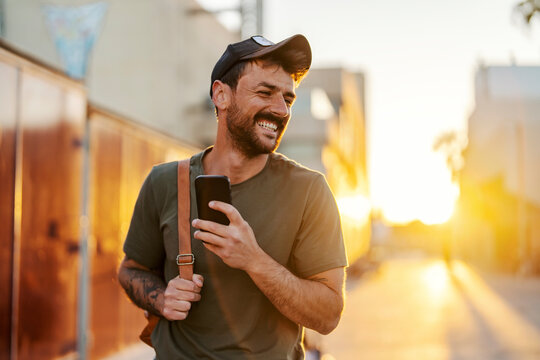 Portrait of a young man walking on a city street downtown at sunset and using his cellphone.