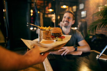 Close up of a hand bringing burger and french fries to a man in a blurry background.