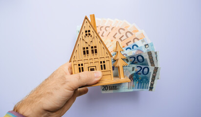 A person holding a house model over a pile of money.