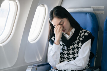 Tired asian woman with headache feeling sick while sitting in the airplane , Passengers near the window. - obrazy, fototapety, plakaty