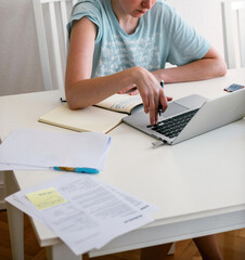 A woman, serene and focused, types on a silver laptop, surrounded by notes, diligently working on her significant PhD project