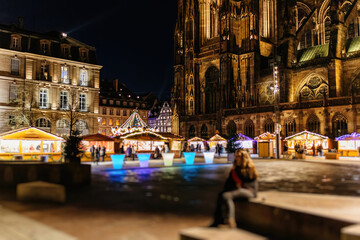 Amidst the lively Christmas market, one person finds serenity on a bench, gazing at the grand Gothic cathedral under the evening sky