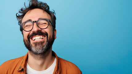 Fototapeta premium Very happy laughing man with glasses in front of blue background with copy space