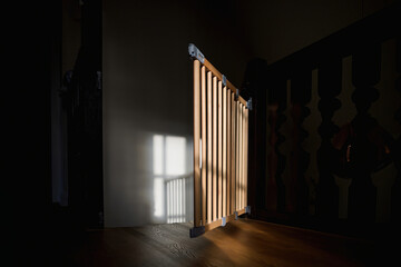 A wooden stair barrier stands open, with sun rays streaming into the dark corridor of a luxury...