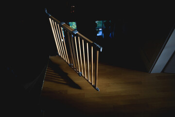 A captivating aerial view of a wooden stair barrier in a luxurious house. Sun rays illuminate the dark corridor, creating a warm and inviting atmosphere