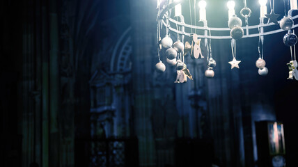 A dimly lit photograph captures an ornate chandelier adorned with figures and stars, hanging inside a cathedral with gothic architecture elements.
