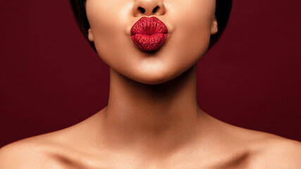 Blowing lips kiss. Young beautiful African american woman make pout lip glitter make up against red...