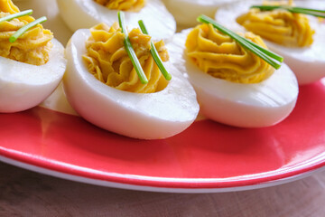 Closeup of stuffed eggs with two sprigs of chives on a plate with a red edge on a wooden table. Image with copy space.	