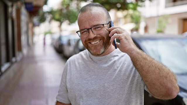 Handsome, bearded caucasian man confidently chatting on his smartphone, positively absorbed in the fun and sunny city street outdoors, portraying a casual, cool lifestyle with warm smile