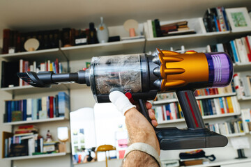 A male hand firmly grips a cordless vacuum cleaner filled with dust inside its transparent plastic receptacle, showcasing the efficient cleaning power.