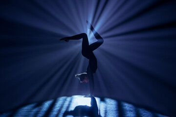Female gymnast on dark background of studio with backlight. Acrobatic girl performing handstand. Modern choreography and acrobatics creative advertising concept. - obrazy, fototapety, plakaty