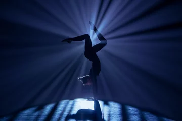 Zelfklevend Fotobehang Female gymnast on dark background of studio with backlight. Acrobatic girl performing handstand. Modern choreography and acrobatics creative advertising concept. © kinomaster