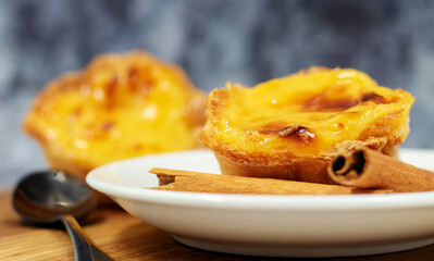 Three Pastel de nata or Portuguese egg tart and cinnamon sticks on a wooden brown background. Pastel de Belem is a small dessert, a cup-shaped pastry made from puff pastry with custard.