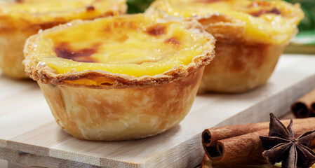 Pastel de nata tarts or Portuguese egg tart on a wooden brown background. Pastel de Belem is a small pie with a crispy puff pastry crust and a custard cream filling. Sweet dessert.
