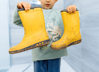 Toddler proudly displaying dirty, mud-covered rubber shoes after an adventurous trail march, showcasing outdoor play