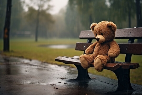 Lonely lost bear on a wooden wet bench in a rainy park. Loneliness concept, International Missing Children's Day