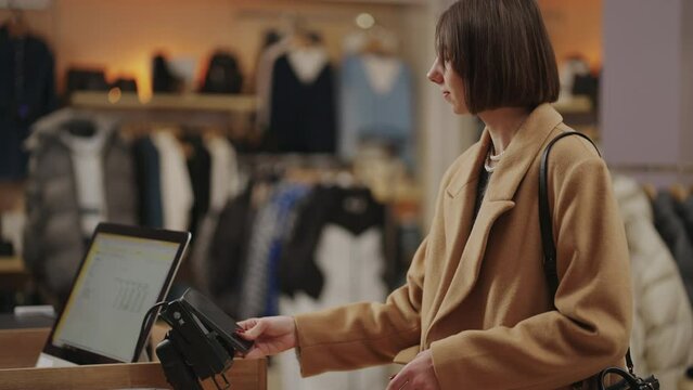 Elegant Businesswoman Purchasing Goods In Clothing Store, Paying By Mobile Phone In Shop Register