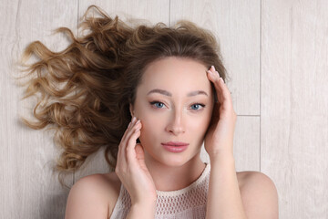 Obraz premium Portrait of beautiful woman with curly hair on wooden floor, top view