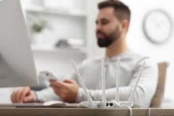 Man with computer and smartphone working at wooden table, focus on Wi-Fi router